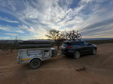 Tracker with rooftop tent and bike rack, hitched to an SUV at sunset